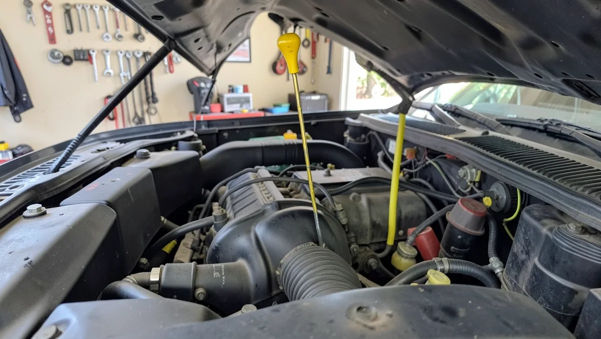 Engine oil dipstick pulled up from an open car engine bay to check the oil level before a trip