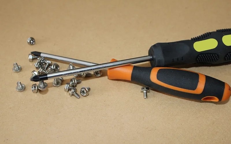Two full-size screwdrivers and loose screws on a brown surface