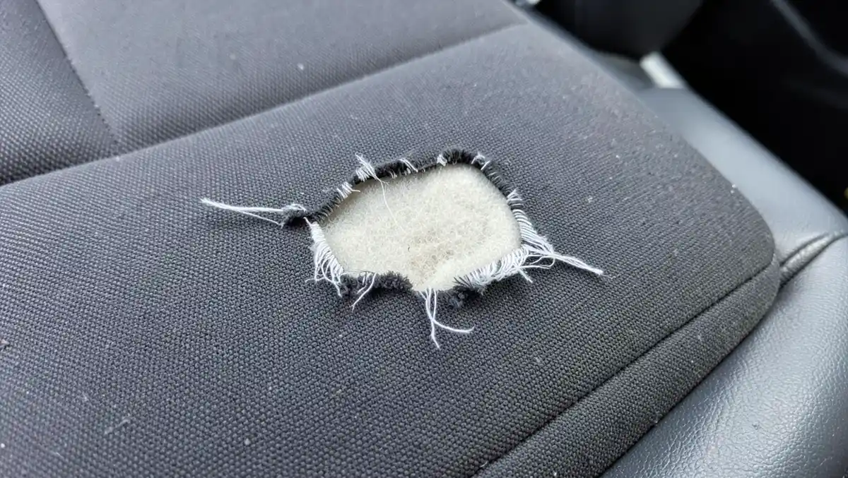 Torn car seat fabric with a visible rip exposing foam padding