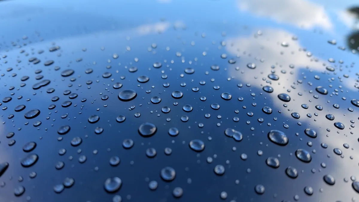 Water droplets beading and rolling off a car windshield with hydrophobic glass coating