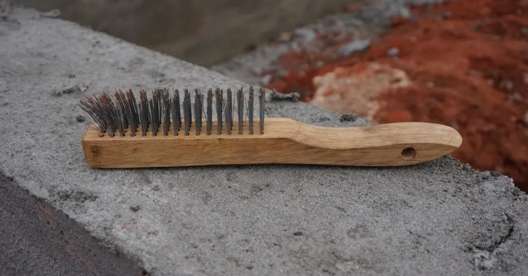 Wire brush with a wooden handle resting on a concrete block, a hand tool for removing loose rust