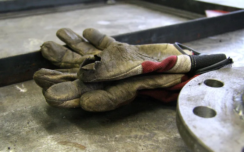 A pair of worn leather work gloves on a metal workbench