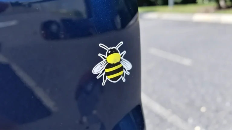 Yellow and black bee-shaped vinyl decal sticker on a dark blue car bumper