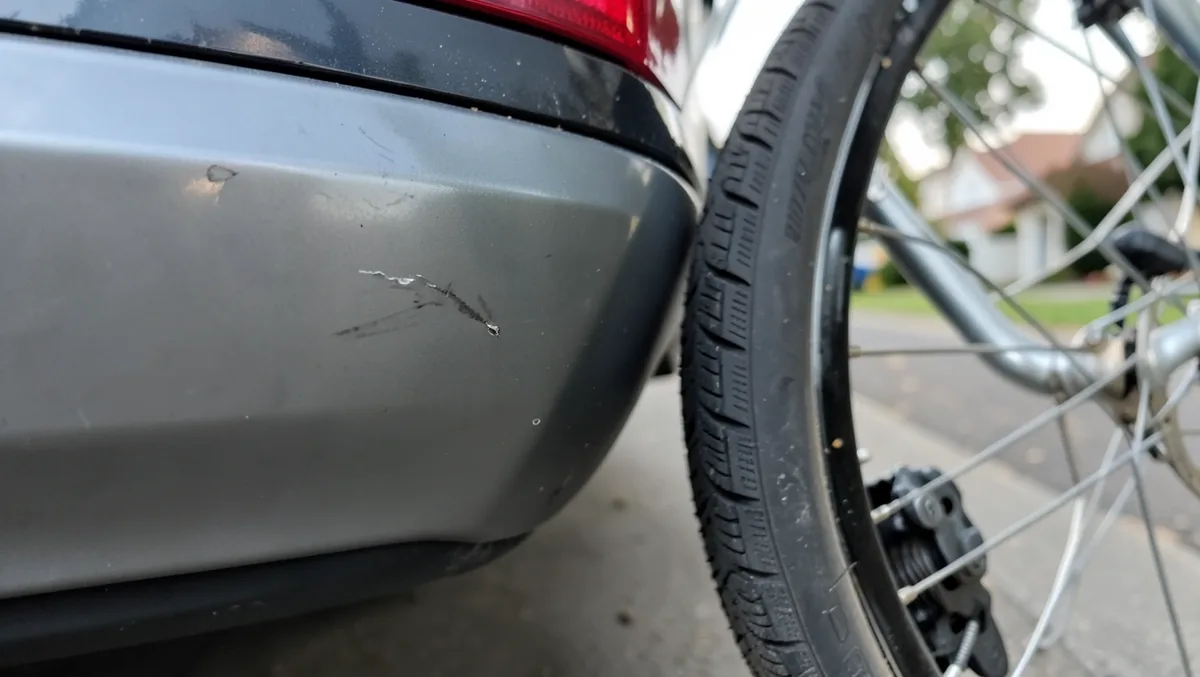 Close-up of a scuffed car bumper next to a bicycle front wheel showing the point of contact