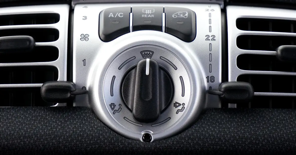 Car dashboard A/C control panel with an A/C button, rear defrost button and temperature dial