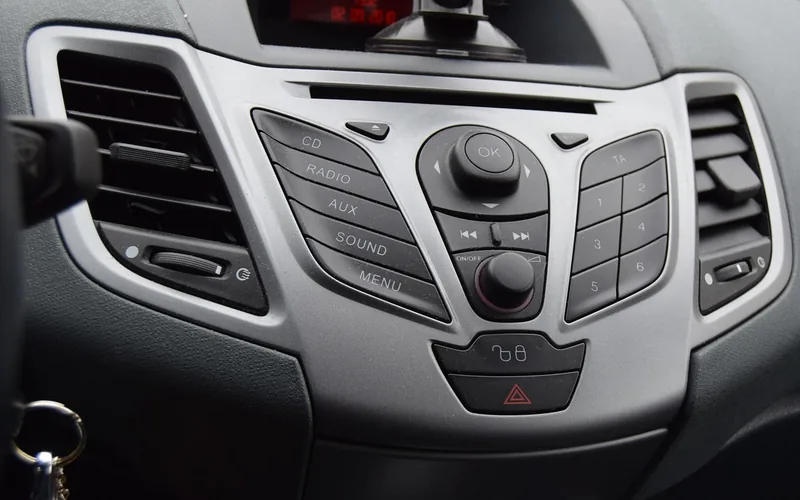 Car dashboard audio controls with CD, radio and AUX buttons below a disc slot