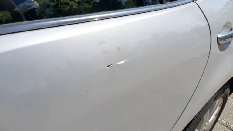 Close-up of a dent and paint scuff on a silver car door panel
