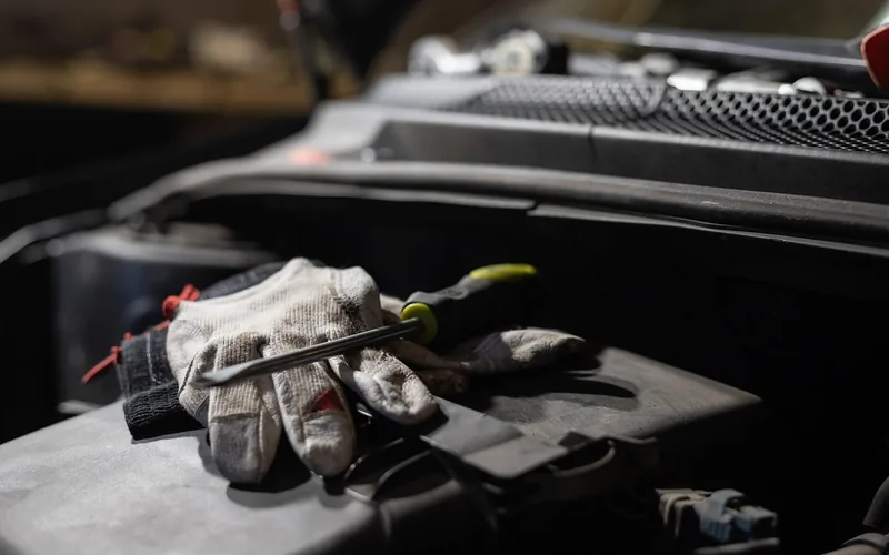 Mechanic using tools to inspect an open car engine bay in a workshop Mechanic using tools to inspect an open car engine bay in a workshop