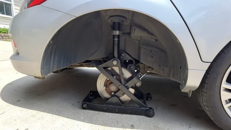 Scissor jack positioned under a sedan rocker panel with the wheel removed to change a tire