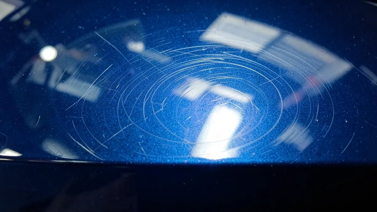 Close-up of fine swirl marks in dark blue car paint reflecting light