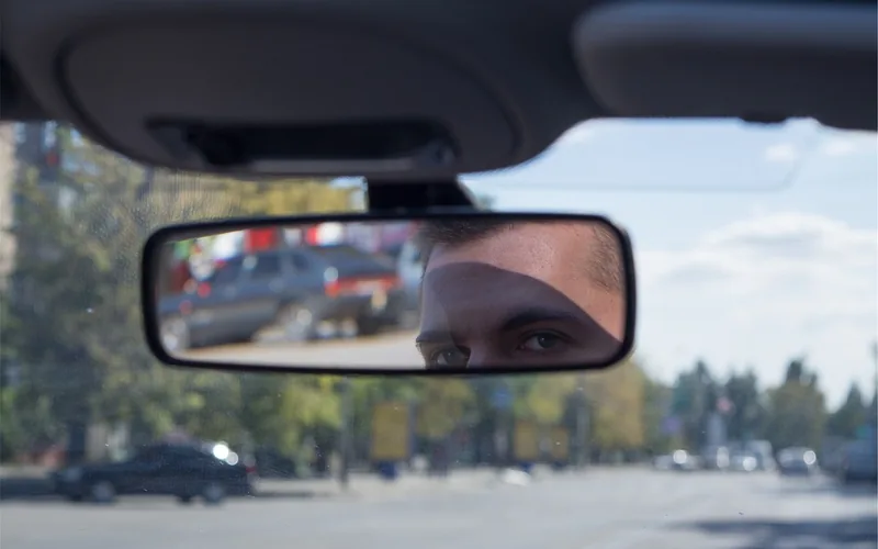Rearview mirror mounted on a car windshield with a street ahead Rearview mirror mounted on a car windshield with a street ahead