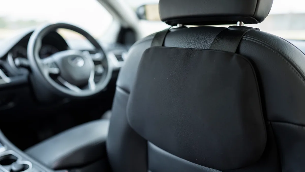 Black lumbar support cushion strapped to a car driver seat backrest for back support
