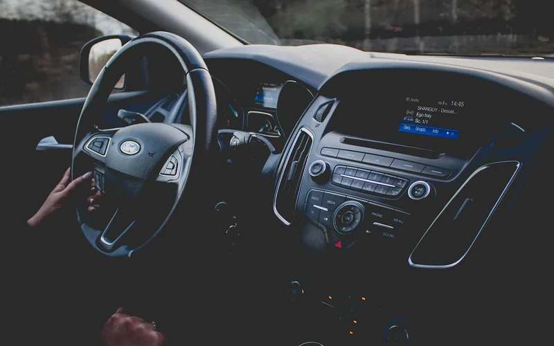 Car stereo display showing the BT Audio source with a track title while driving