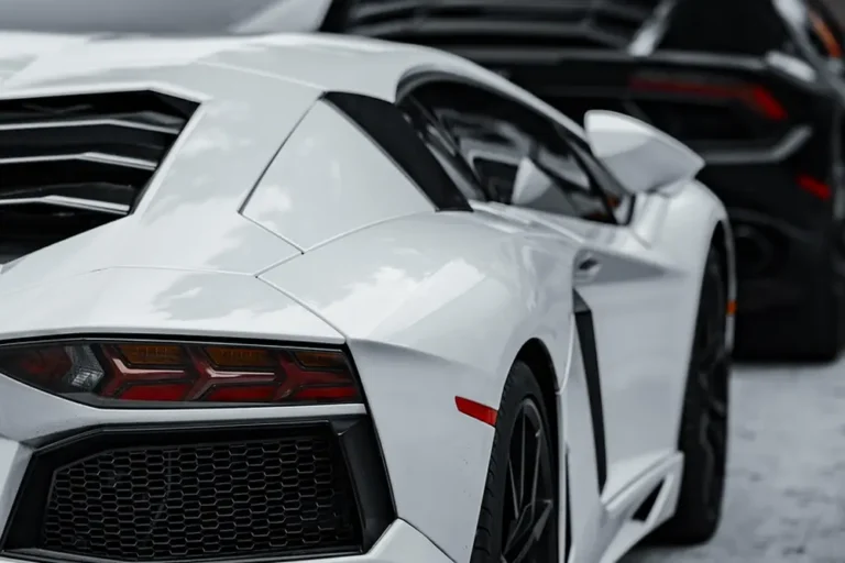 White sports car with black car behind it, rear three-quarter view