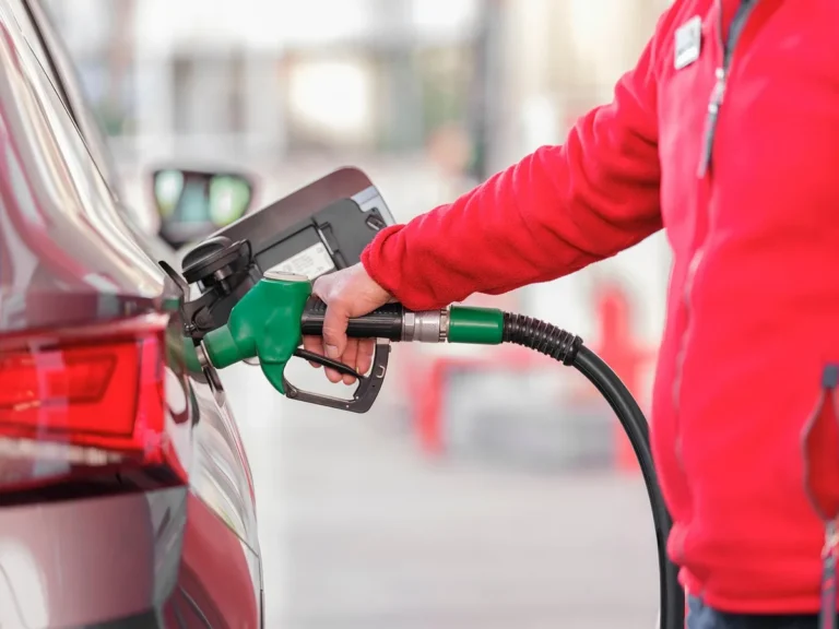 Hand holding a green fuel nozzle in a car fuel filler at a gas station