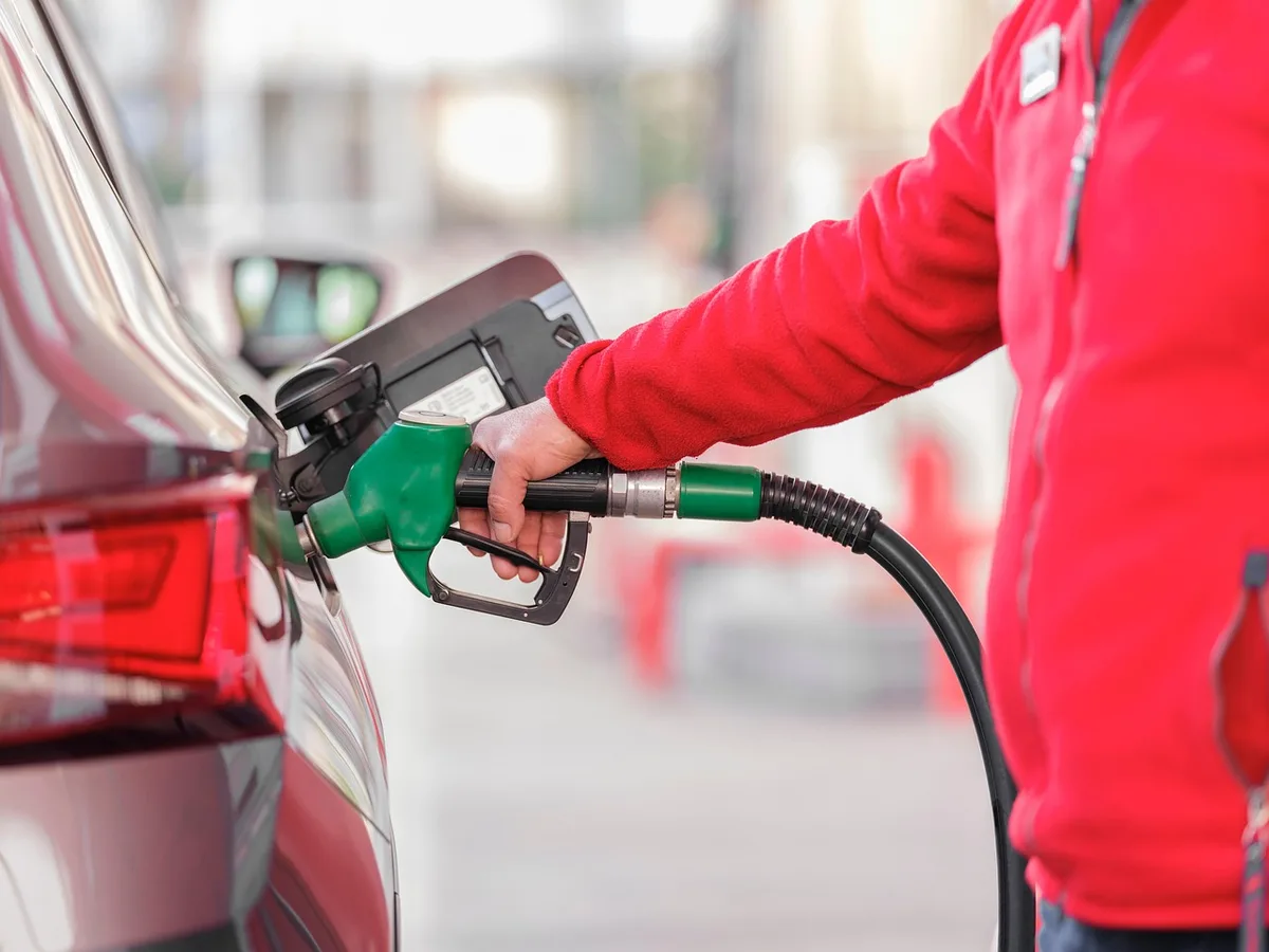 Hand holding a green fuel nozzle in a car fuel filler at a gas station