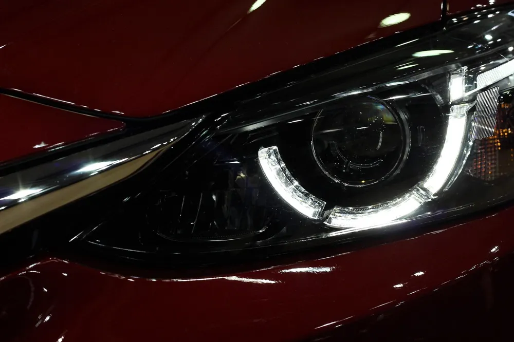 Close view of a lit LED car headlight on a dark red car