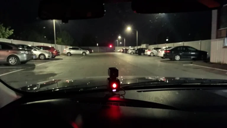 Dash cam mounted on a windshield recording an empty nighttime parking lot in parking mode