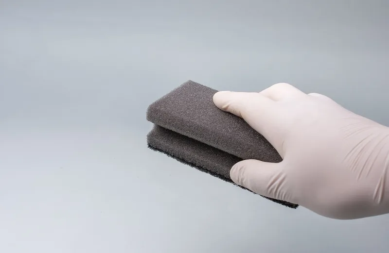Gloved hand holding a dark sponge pad