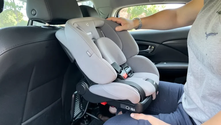 Parent lifting a Graco infant car seat carrier off its detachable base in the back seat of a car