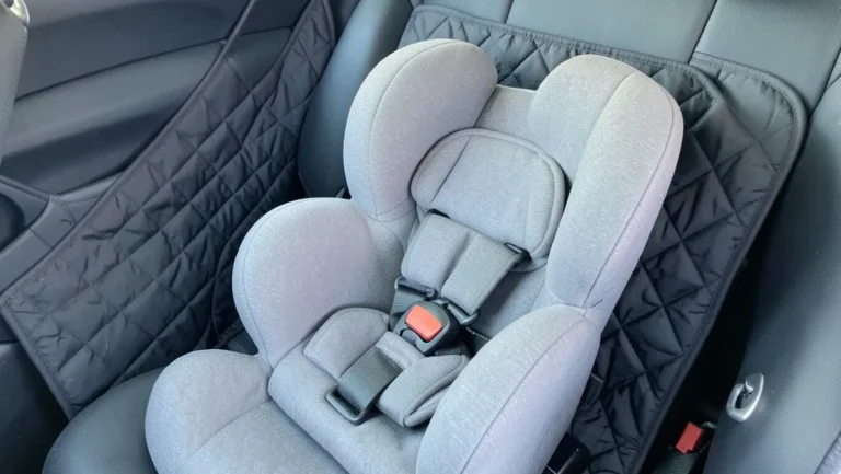 Convertible child car seat installed over a quilted seat protector mat in the back seat of a car