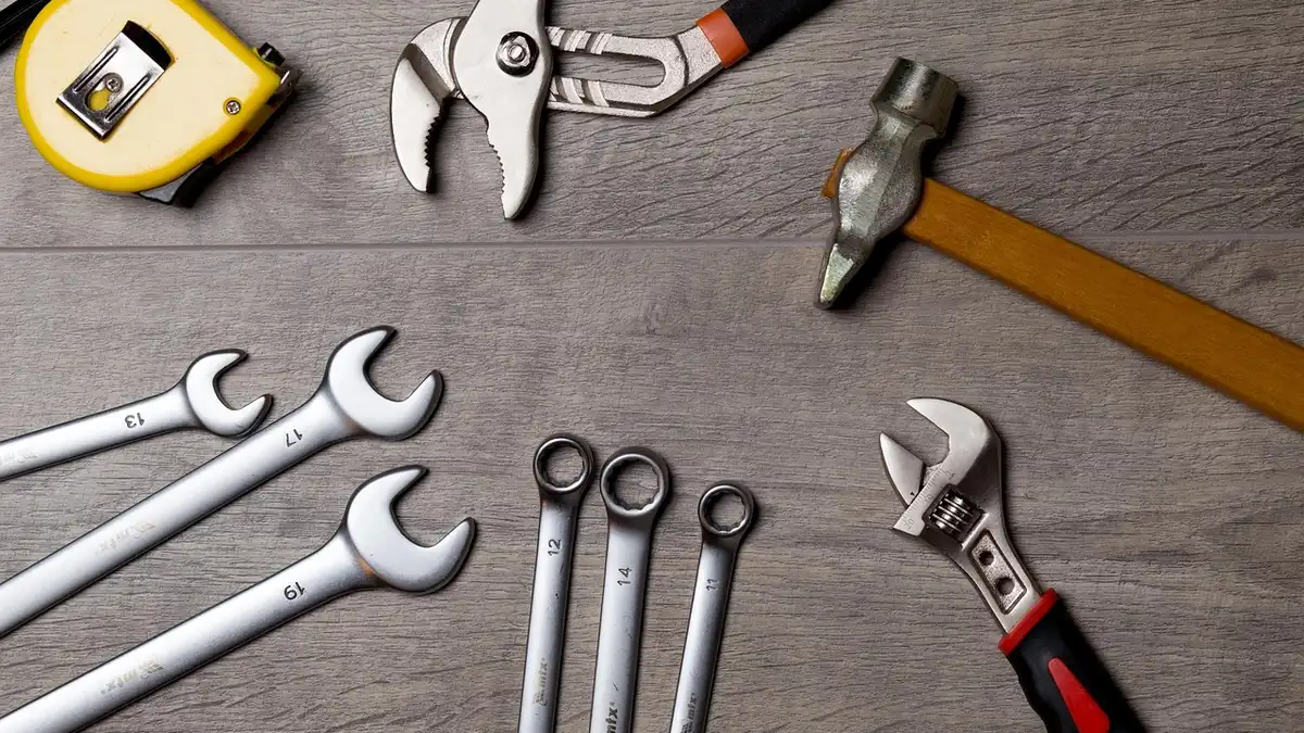 Flat lay of wrenches, pliers, a hammer and a tape measure on a gray wood surface