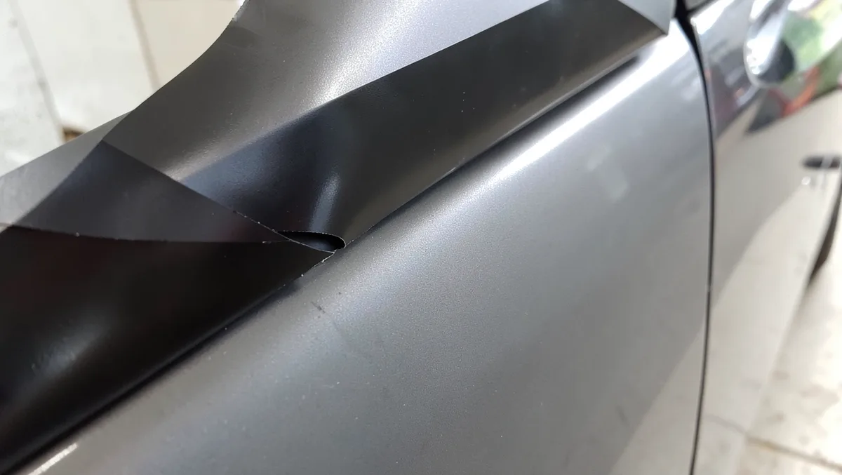Corner of black vinyl car wrap peeling away from a car door panel