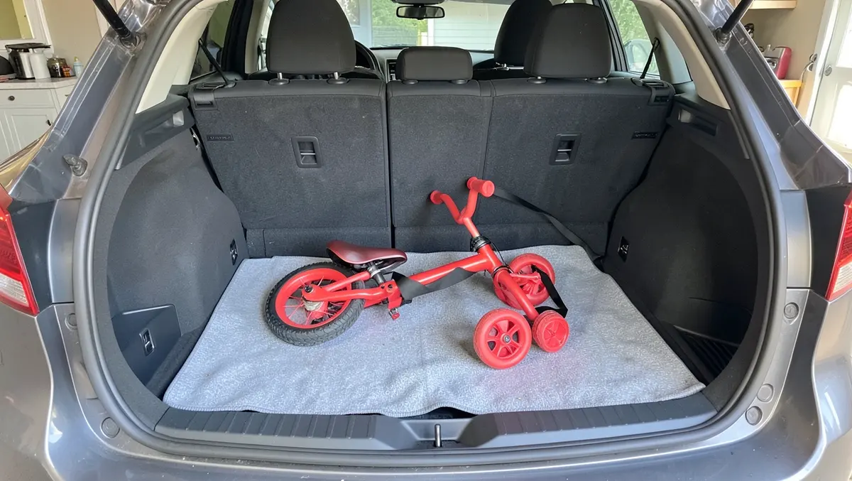 Small children's tricycle laid flat and strapped down inside an open car trunk on a blanket