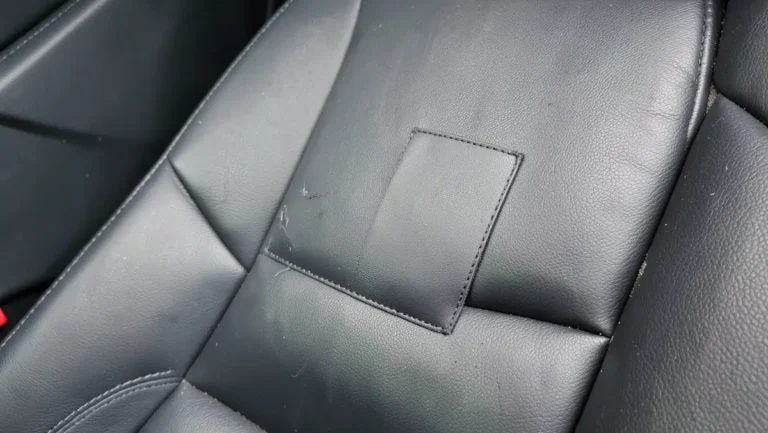 Close-up of a black leather car seat bolster with a repair patch applied over a small tear