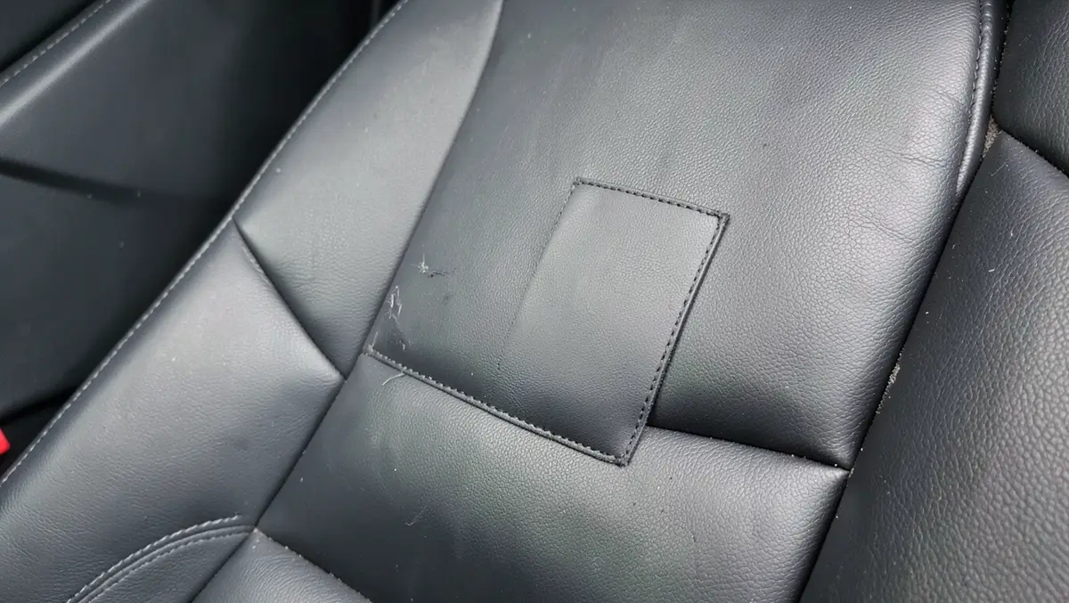 Close-up of a black leather car seat bolster with a repair patch applied over a small tear