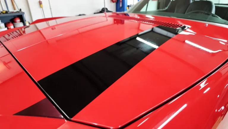 Black vinyl racing stripe decal applied to a red car hood