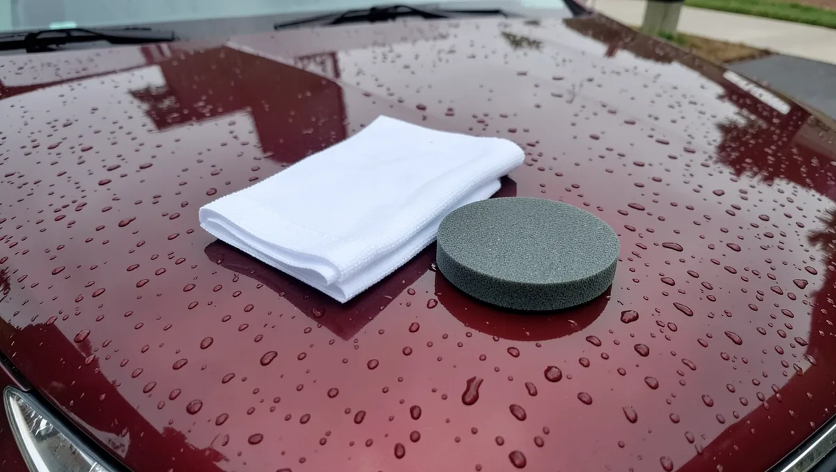Microfiber cloth and foam wax applicator pad on a freshly washed wet car hood