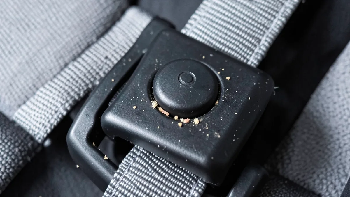 Close-up of a child car seat harness adjuster button with food crumbs caught around the mechanism