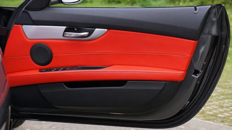 Open car door showing a red leather-look door panel with a speaker and window switches