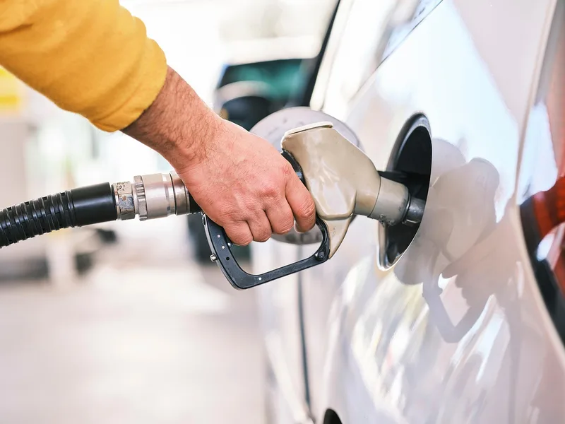 Hand holding a fuel nozzle while refueling a white car at a gas station