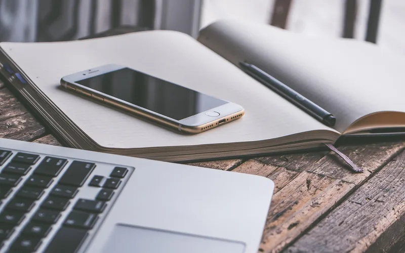 Smartphone resting on an open notebook beside a laptop keyboard