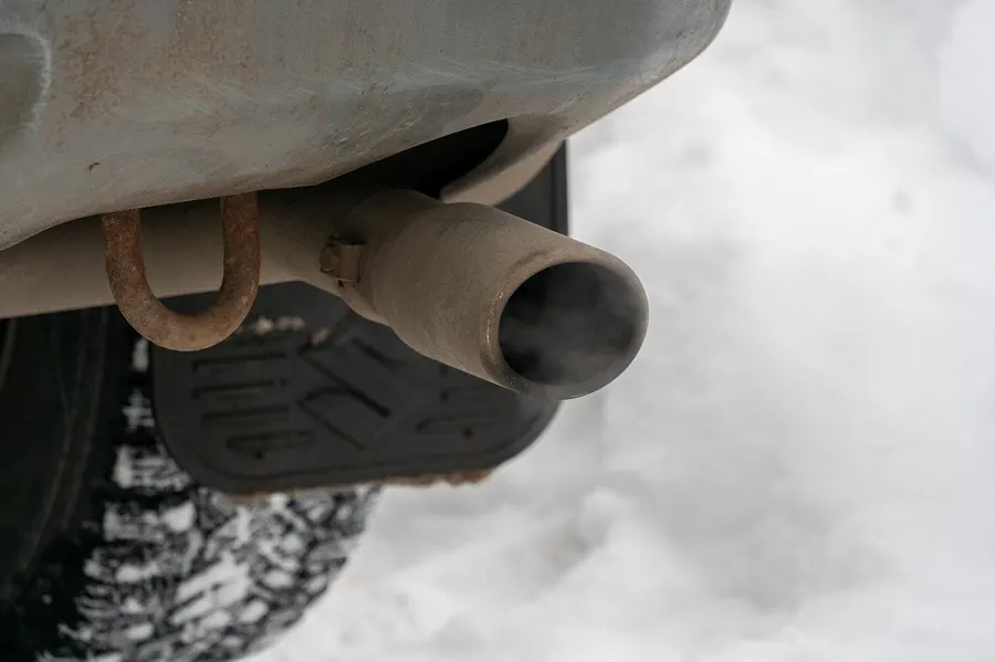 Car tailpipe in snow with a faint haze of exhaust at the opening