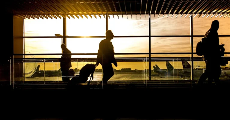 Travelers walking with luggage through an airport terminal at sunset