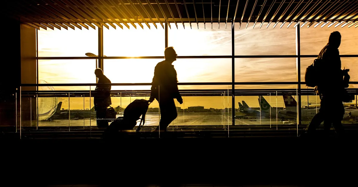 Travelers walking with luggage through an airport terminal at sunset