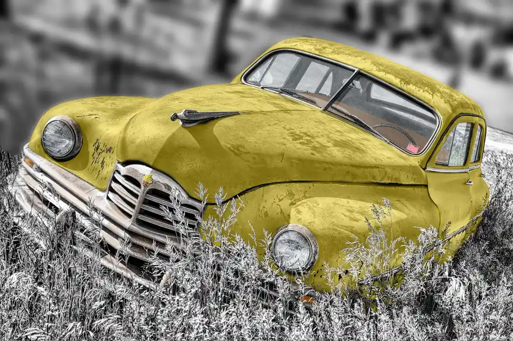 Weathered yellow vintage car with a worn hood, seen from the front corner