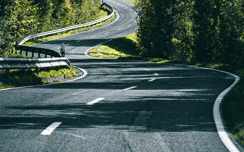 Winding two-lane country road with a guardrail and dashed center line
