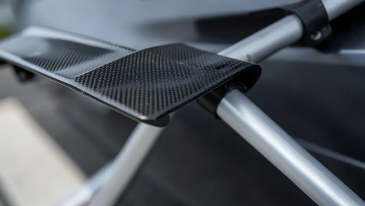 Close-up of a raised carbon fiber wing spoiler mounted on adjustable aluminum struts