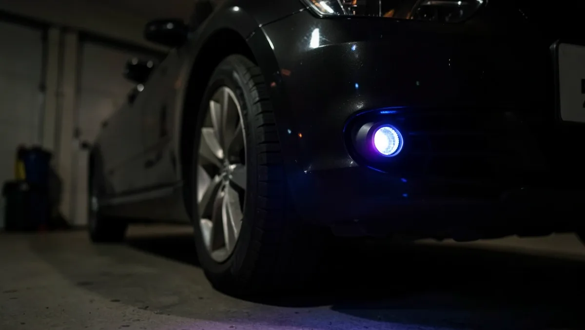 Wireless LED accent puck light glowing blue near a car front bumper at night