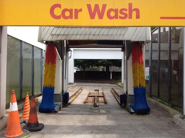 Entrance to an automatic car wash tunnel with red, yellow, and blue spinning brushes and a Car Wash sign