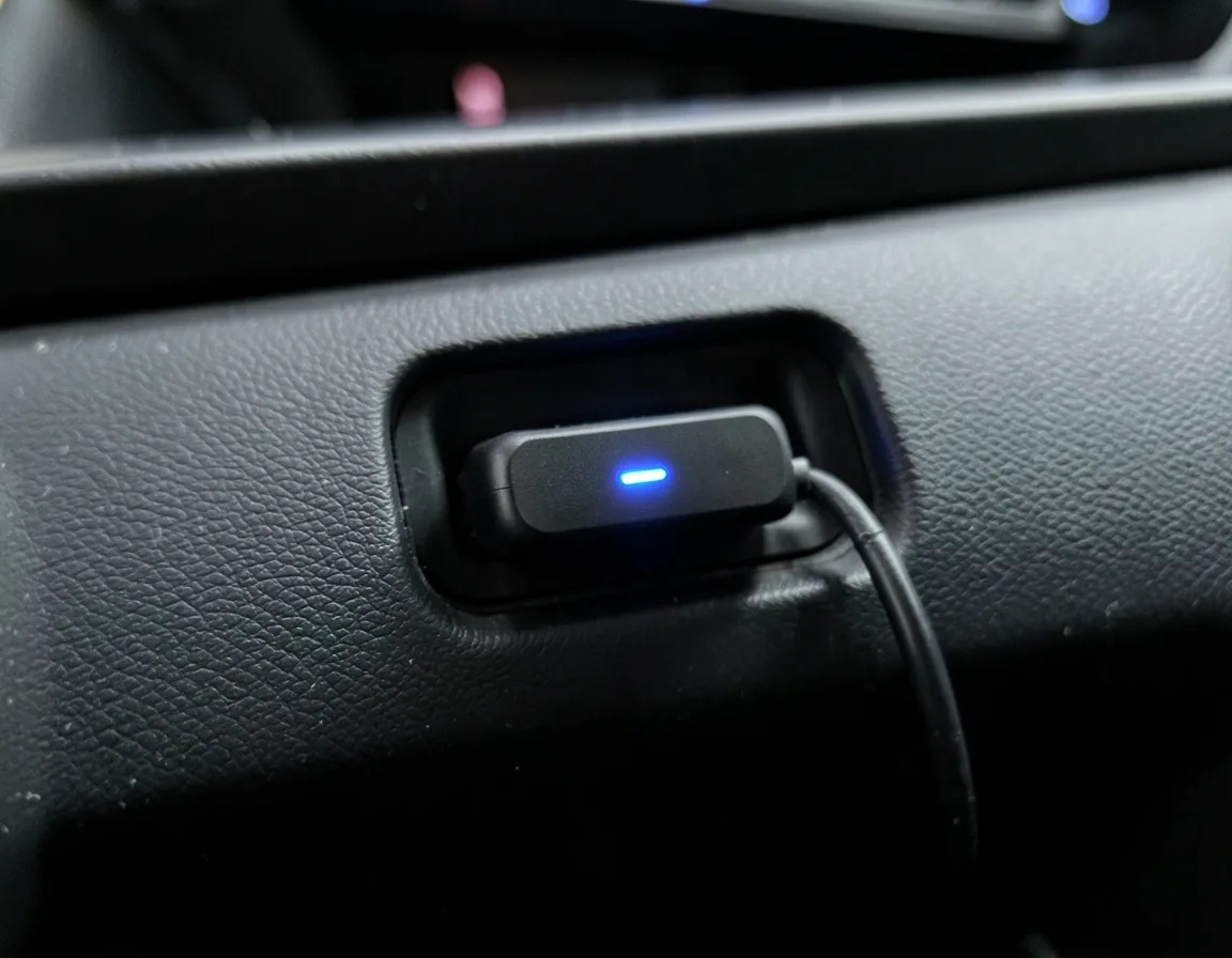Small bluetooth audio receiver plugged into a car dashboard aux port with its LED indicator lit