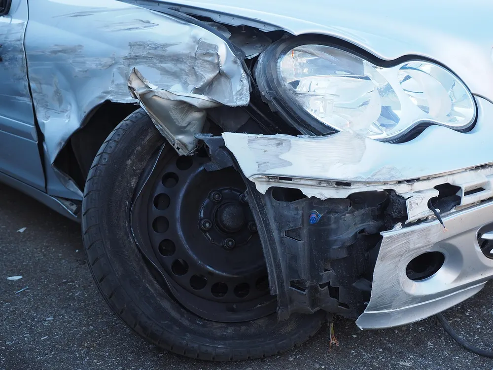 Front corner of a silver car with a cracked and detached plastic bumper cover