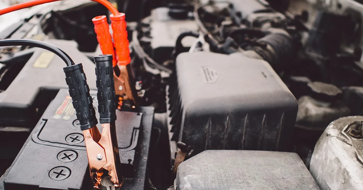 Jumper cables clamped to a car battery terminal under an open hood Jumper cables clamped to a car battery terminal under an open hood