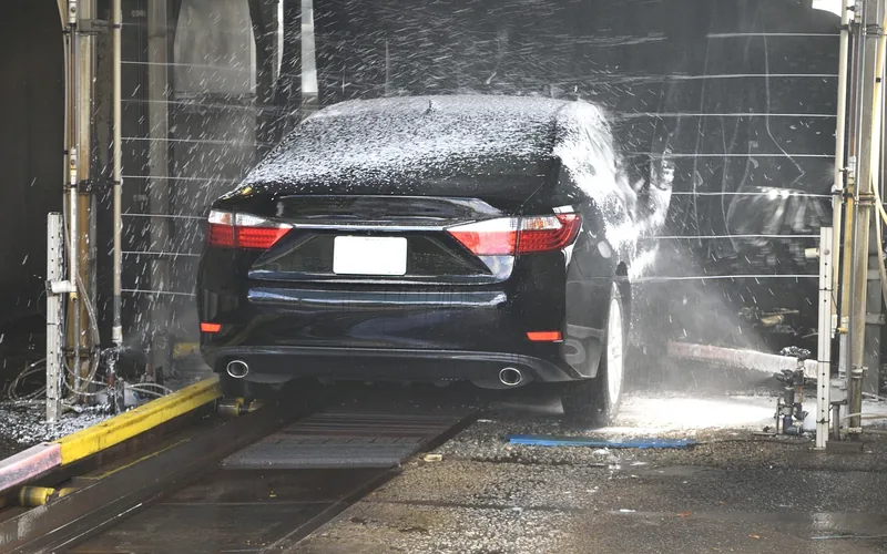 sedan being rinsed with a high-pressure spray wand at a car wash