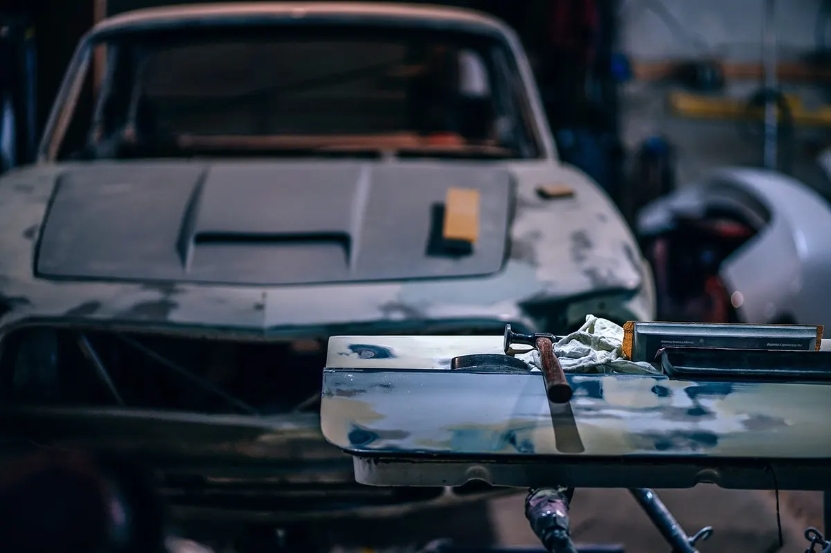 Car body panel with sanding blocks and a hammer on a workshop bench