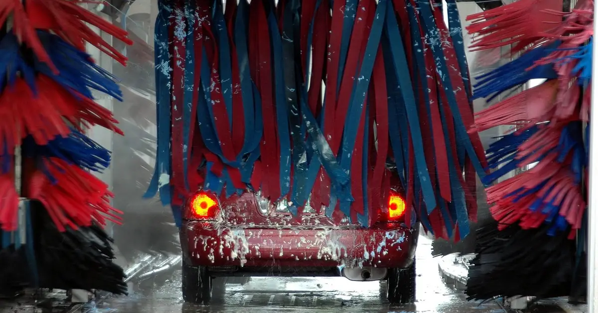Car going through an automatic car wash tunnel between rows of red and blue brushes